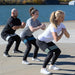 Three people performing a workout routine by a waterfront using some resistance bands.